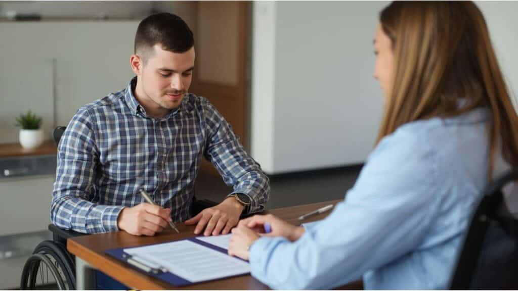 בחור צעיר אחרי תאונת עבודה חותם על מסמכי תביעת ביטוח מול עורך דין אובדן כושר עבודה כדי להגיש תביעת ביטוח